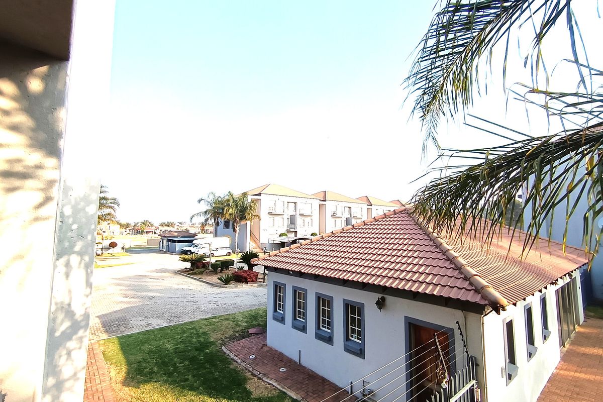 An elevated view of the apartment complex grounds, featuring a tiled-roof building, paved driveway, and well-maintained garden areas with security fencing.