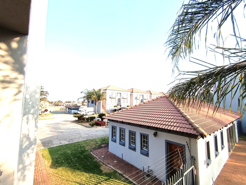 An elevated view of the apartment complex grounds, featuring a tiled-roof building, paved driveway, and well-maintained garden areas with security fencing.