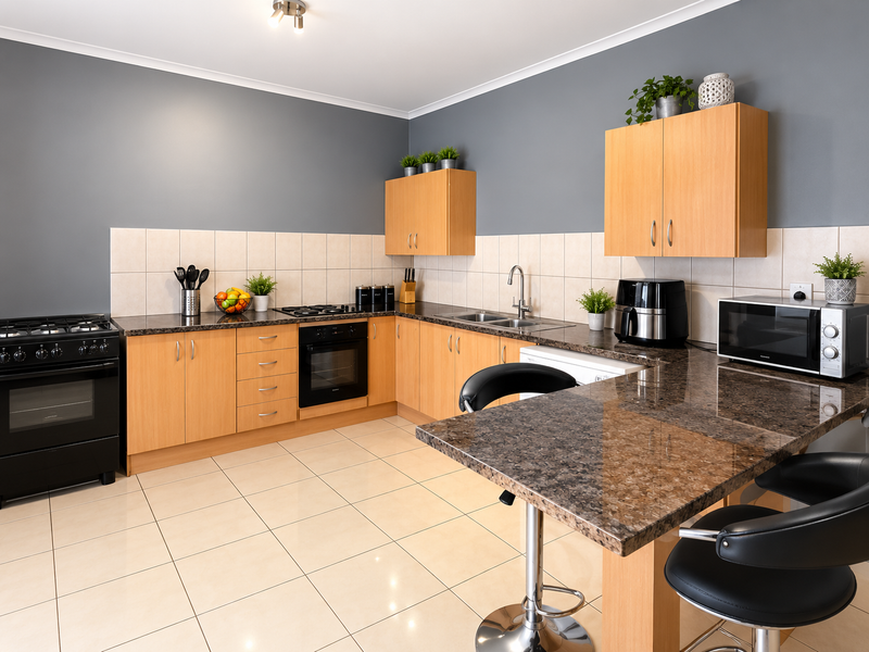A well-maintained kitchen featuring light wood cabinetry, granite countertops, a breakfast bar, and integrated appliances with a neutral tiled backsplash and flooring.