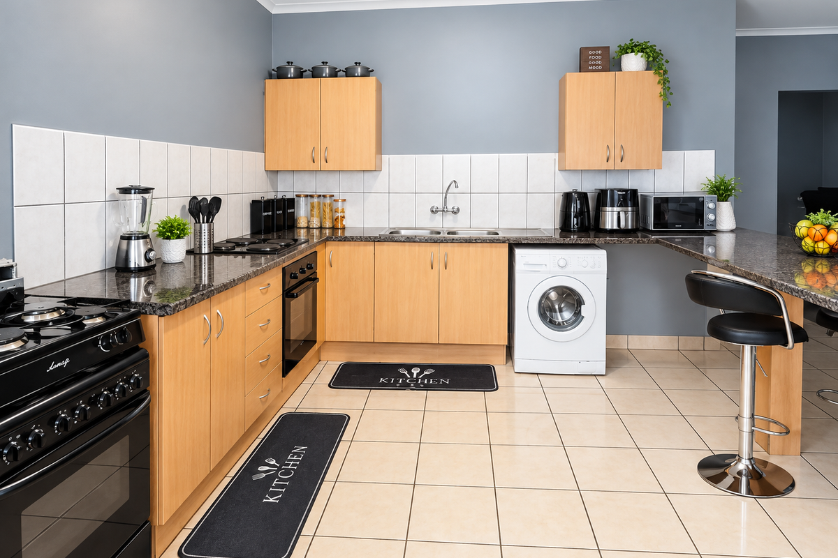 Functional kitchen featuring light wood cabinetry, granite countertops, tiled backsplash, built-in oven, and an integrated washing machine with a breakfast bar area.