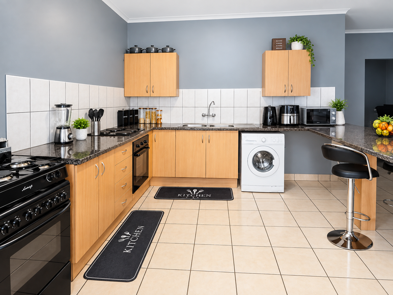 Functional kitchen featuring light wood cabinetry, granite countertops, tiled backsplash, built-in oven, and an integrated washing machine with a breakfast bar area.
