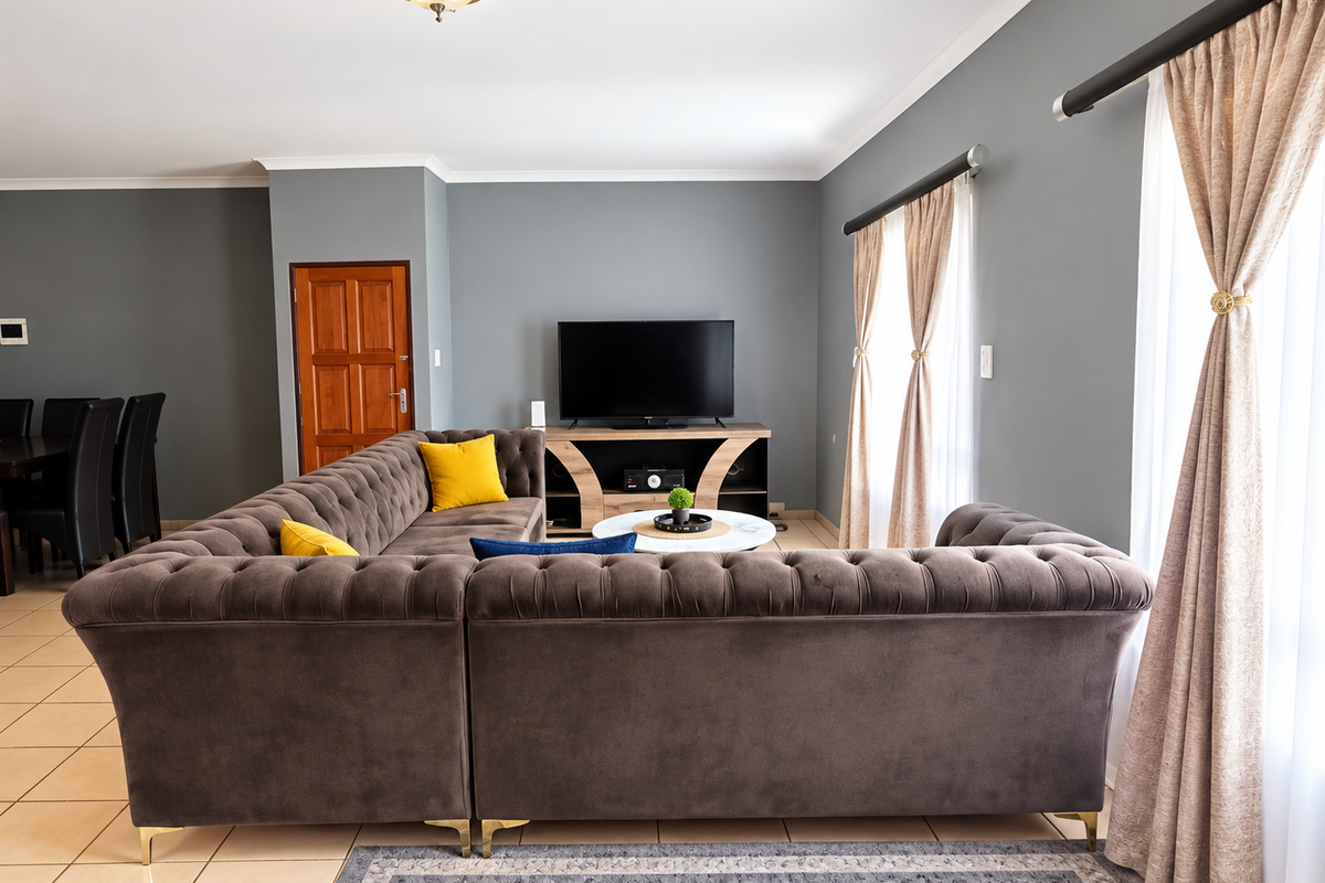 A well-maintained living room featuring neutral grey walls, tiled flooring, and large windows with elegant curtain treatments.