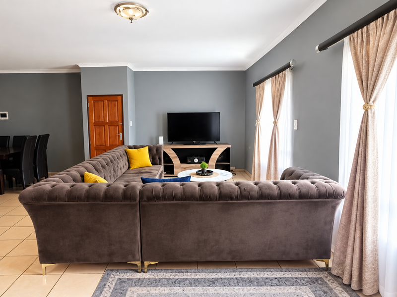 A well-maintained living room featuring neutral grey walls, tiled flooring, and large windows with elegant curtain treatments.
