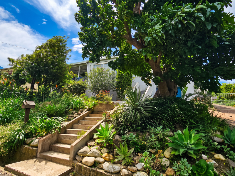 Front exterior view featuring a landscaped garden, concrete staircase leading to the entrance, and a paved driveway with metal gate access.