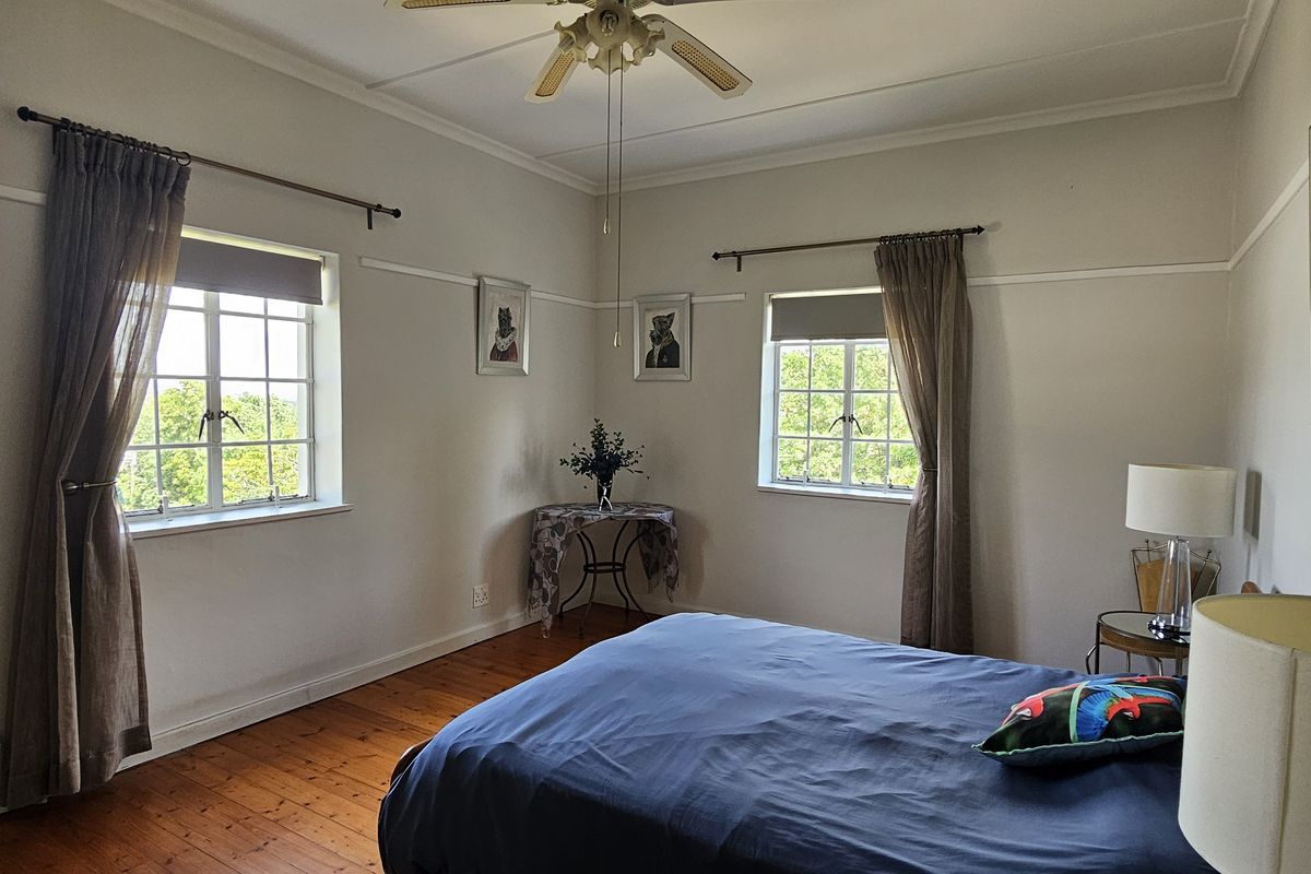 A well-lit bedroom featuring original timber flooring, classic picture rails, and dual casement windows providing natural light.