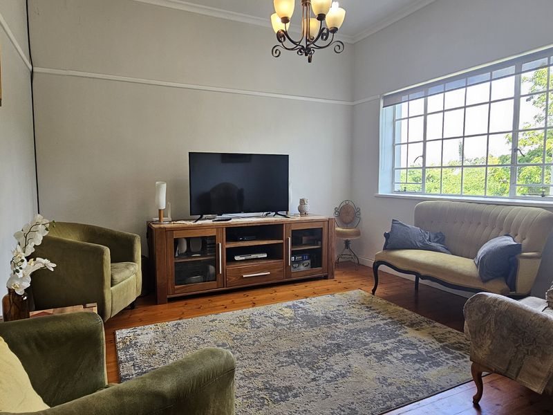A well-lit living room featuring original hardwood flooring, a classic picture rail, and a large multi-pane window providing natural light.