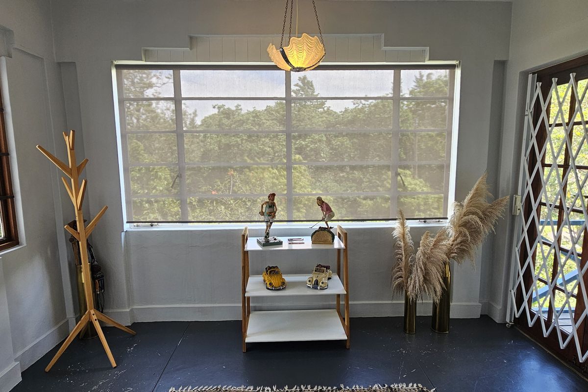 A bright living area featuring timber-framed windows, security gates, and a central pendant light, offering a view of the surrounding greenery.