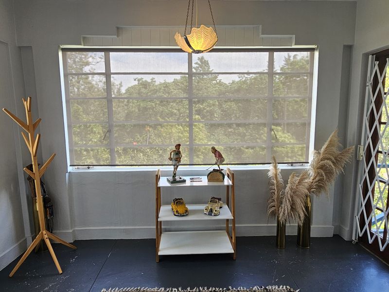 A bright living area featuring timber-framed windows, security gates, and a central pendant light, offering a view of the surrounding greenery.