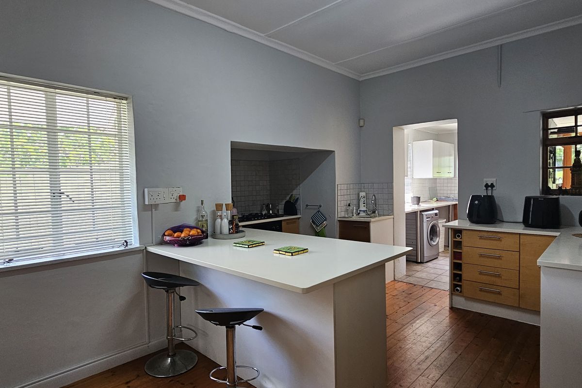 Functional kitchen featuring timber flooring, ample built-in cabinetry, a breakfast bar, and a convenient adjoining scullery area.
