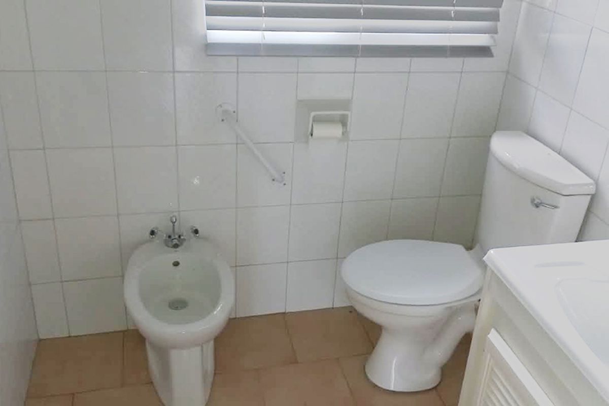 A functional bathroom featuring a toilet, bidet, wall-mounted grab rail, and a vanity cabinet with tiled wall finishes.