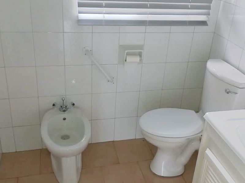 A functional bathroom featuring a toilet, bidet, wall-mounted grab rail, and a vanity cabinet with tiled wall finishes.