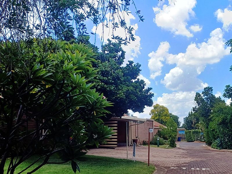 Front view of a retirement village property featuring a brick facade, paved driveway, and established garden surroundings.