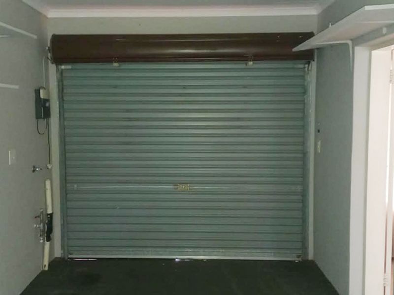 A functional garage space featuring a secure roller shutter door, wall-mounted shelving units, and existing plumbing connections for utility use.