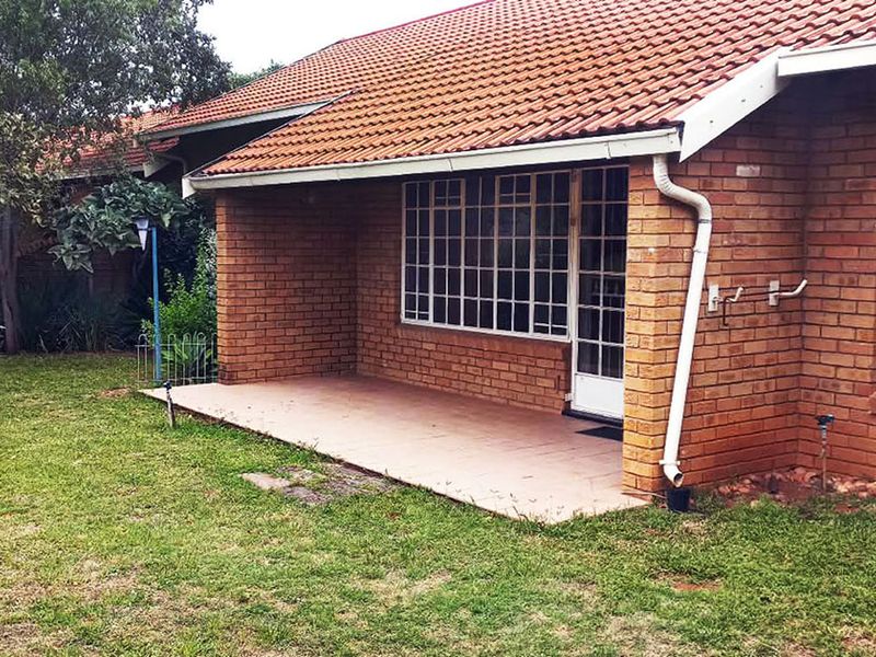 Rear view of a retirement village unit featuring a face brick facade, tiled patio area, and established garden space.