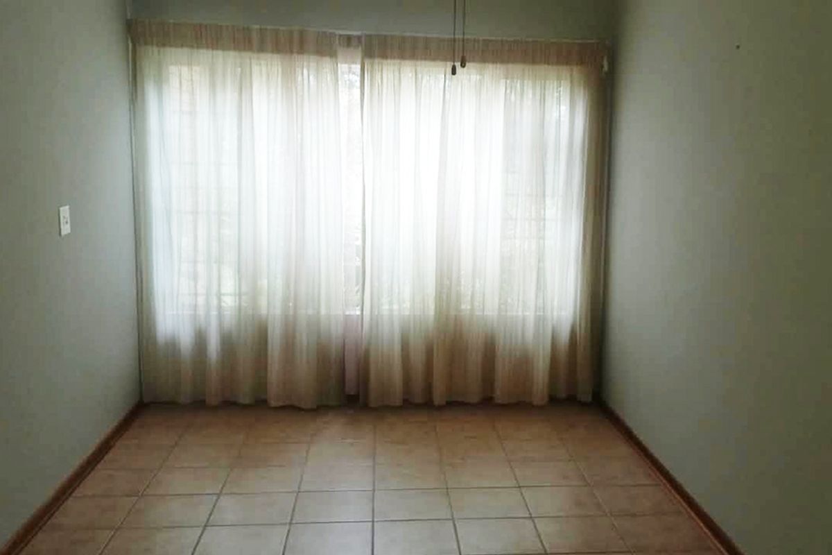 An empty bedroom featuring neutral tiled flooring and large window coverage, providing a blank canvas for personalization in this retirement village unit.