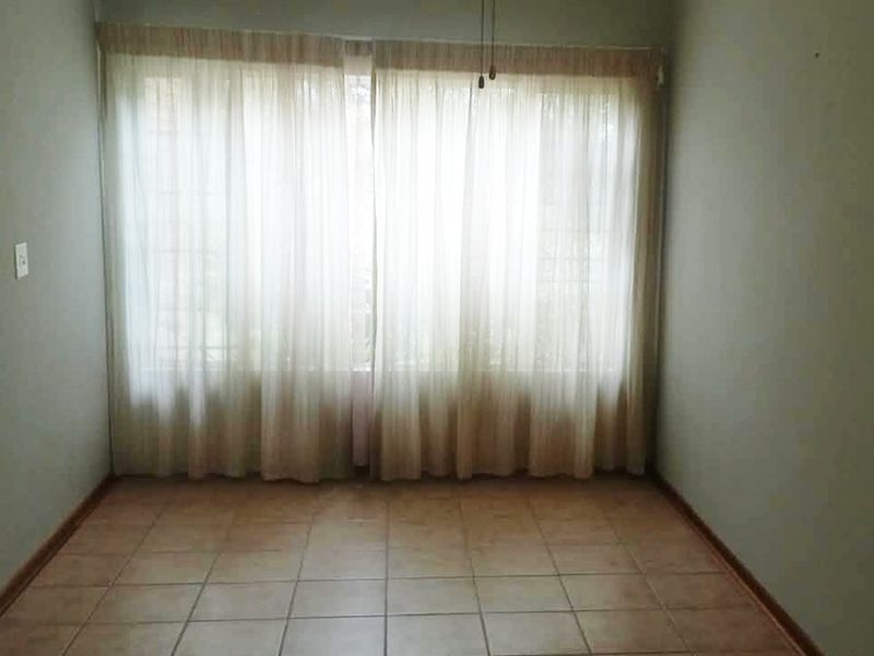 An empty bedroom featuring neutral tiled flooring and large window coverage, providing a blank canvas for personalization in this retirement village unit.