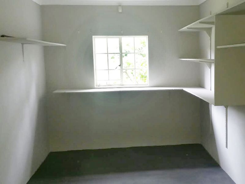 A functional utility space or storage room featuring built-in shelving and a central window, providing a clean and versatile area for various uses.
