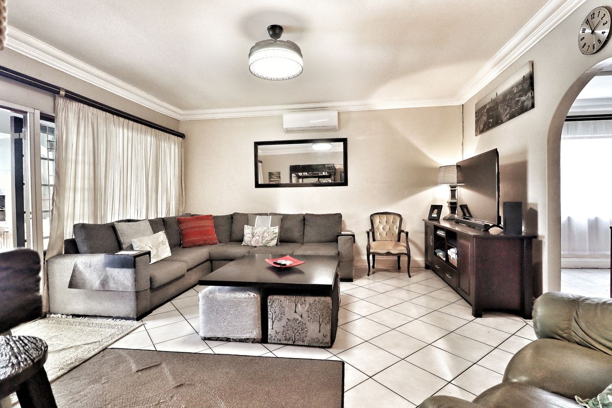 A spacious living room featuring tiled flooring, a split-system air conditioner, and a decorative archway leading to adjacent areas.