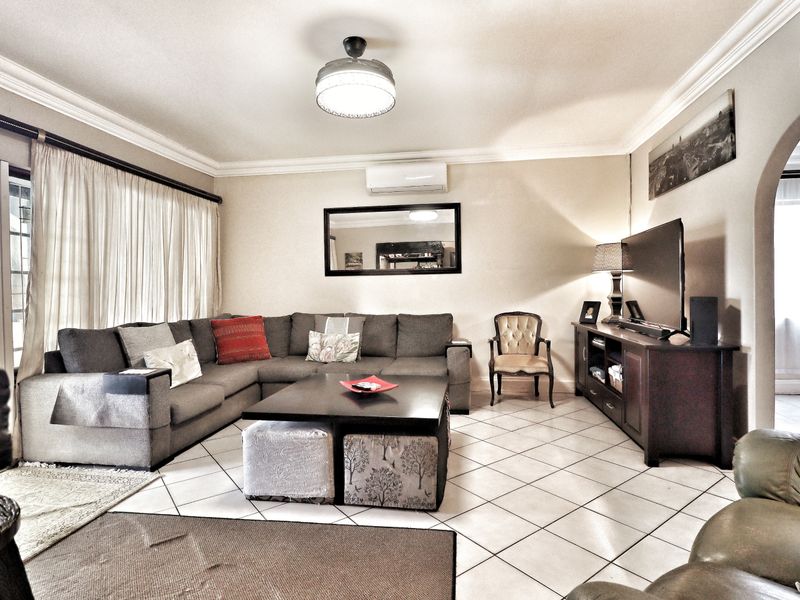 A spacious living room featuring tiled flooring, a split-system air conditioner, and a decorative archway leading to adjacent areas.