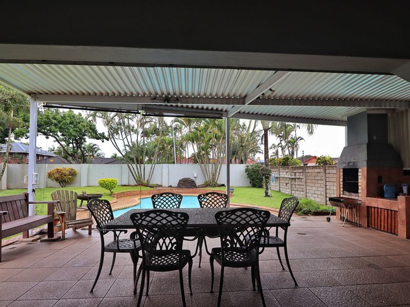 Covered outdoor patio featuring a built-in brick braai, tiled flooring, and direct access to the garden and swimming pool area.