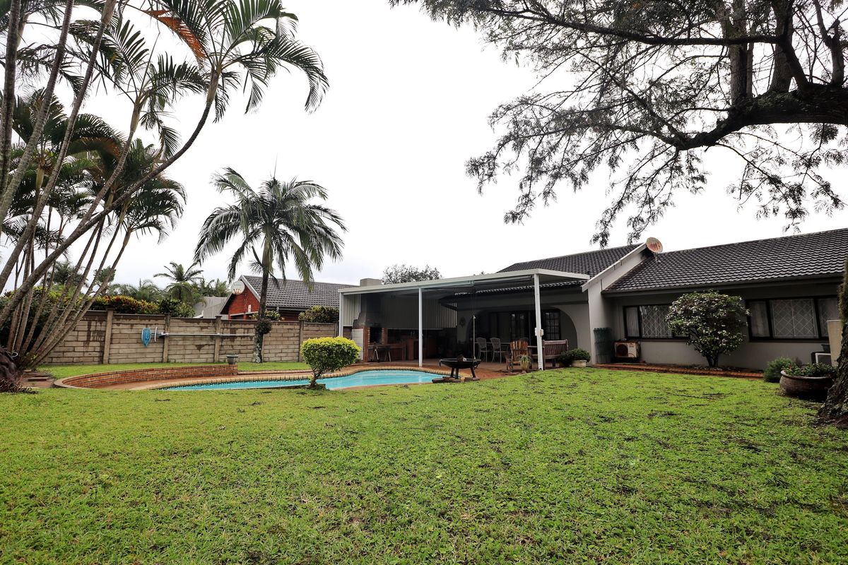 Spacious rear garden featuring a swimming pool, paved surround, and a covered patio area with a built-in braai, perfect for outdoor entertaining.