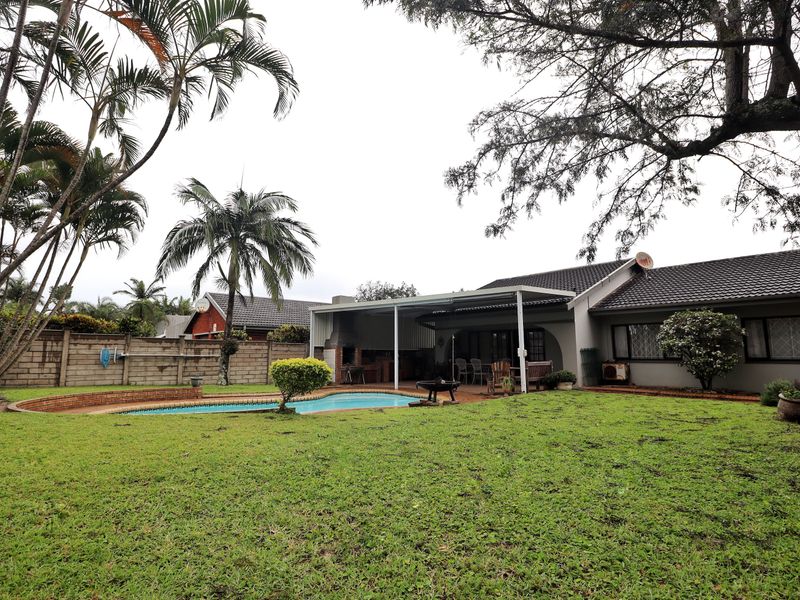 Spacious rear garden featuring a swimming pool, paved surround, and a covered patio area with a built-in braai, perfect for outdoor entertaining.
