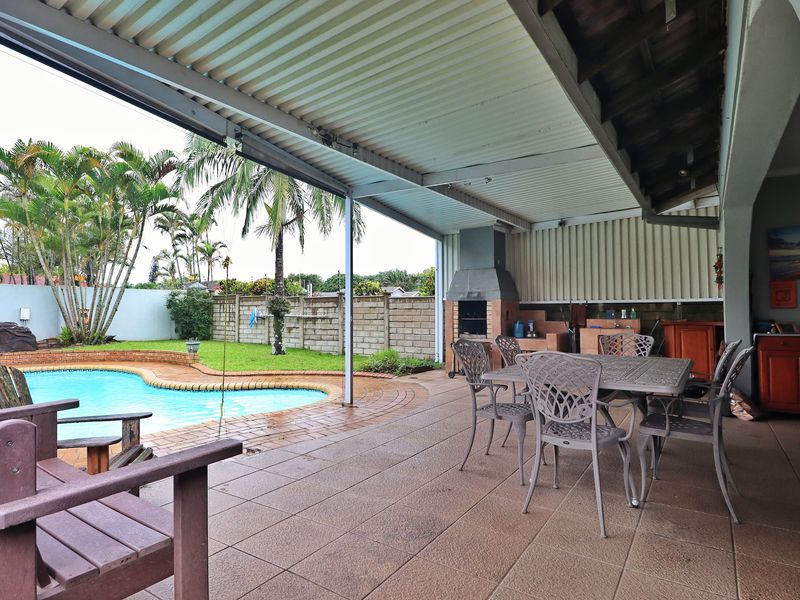 Covered outdoor patio featuring a built-in braai, tiled flooring, and direct access to a swimming pool and garden area.