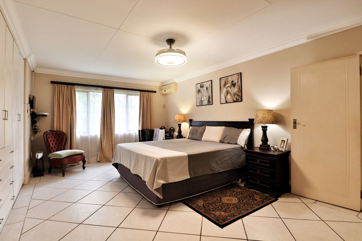 Spacious bedroom featuring tiled flooring, built-in cupboards, a ceiling fan, and an integrated air conditioning unit.