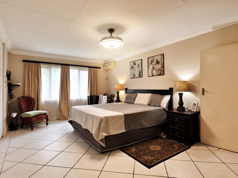 Spacious bedroom featuring tiled flooring, built-in cupboards, a ceiling fan, and an integrated air conditioning unit.