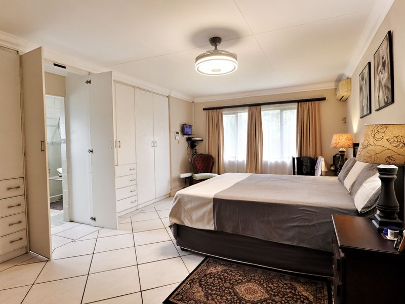 Spacious bedroom featuring built-in cupboards, tiled flooring, a ceiling fan, and an air conditioning unit, with convenient access to an en-suite bathroom.