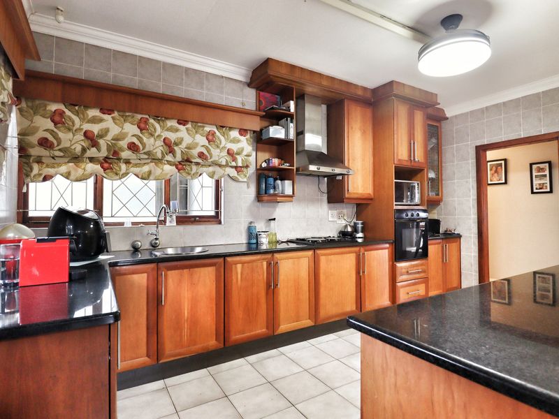 A functional kitchen featuring warm wooden cabinetry, granite countertops, a built-in oven, gas hob, and a stainless steel extractor fan with tiled finishes.