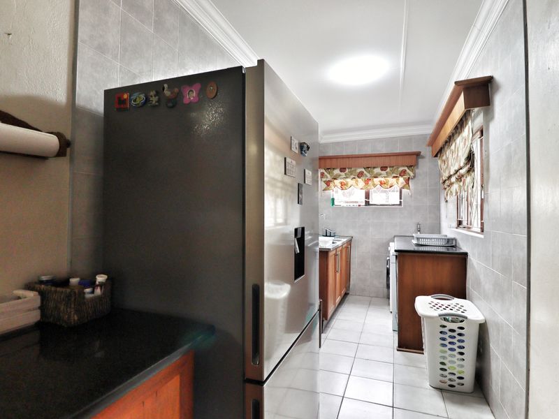 A functional scullery featuring tiled walls, granite countertops, and built-in wooden cabinetry, providing additional prep and wash-up space.