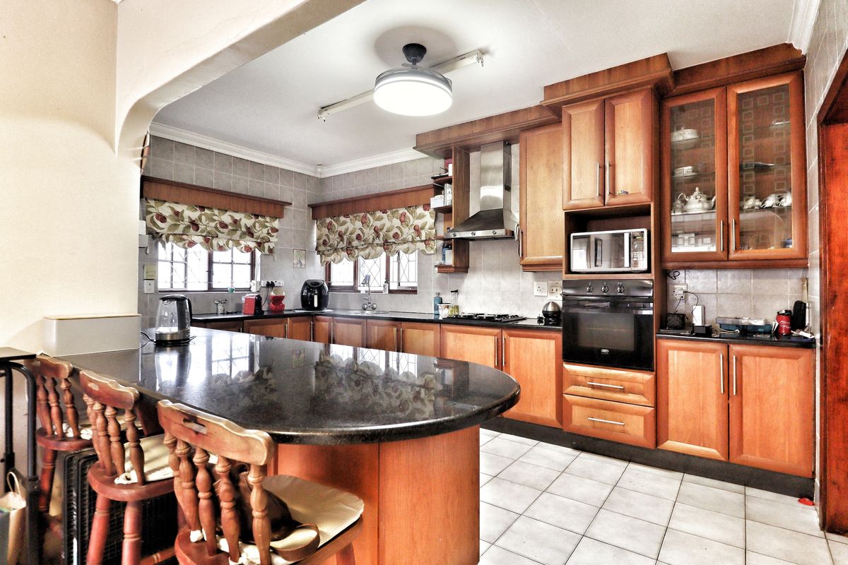 A functional kitchen featuring wooden cabinetry, granite countertops, a breakfast bar, and built-in appliances including an oven, microwave, and extractor fan.