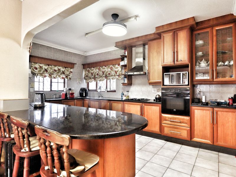 A functional kitchen featuring wooden cabinetry, granite countertops, a breakfast bar, and built-in appliances including an oven, microwave, and extractor fan.