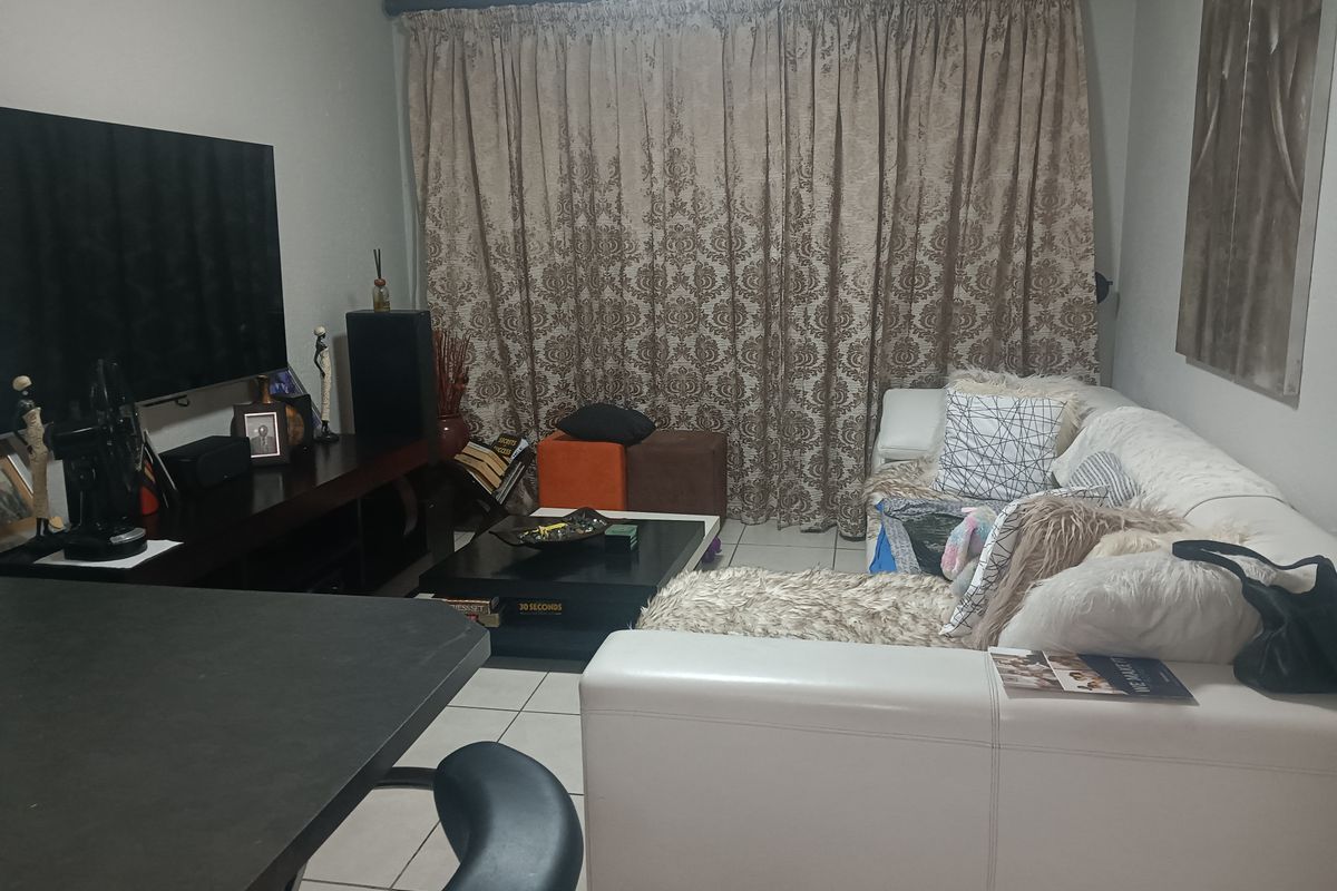 A functional living room area featuring tiled flooring and a large window covered by curtains.