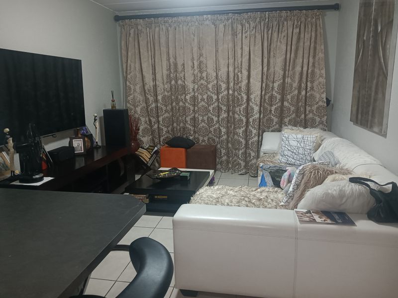 A functional living room area featuring tiled flooring and a large window covered by curtains.