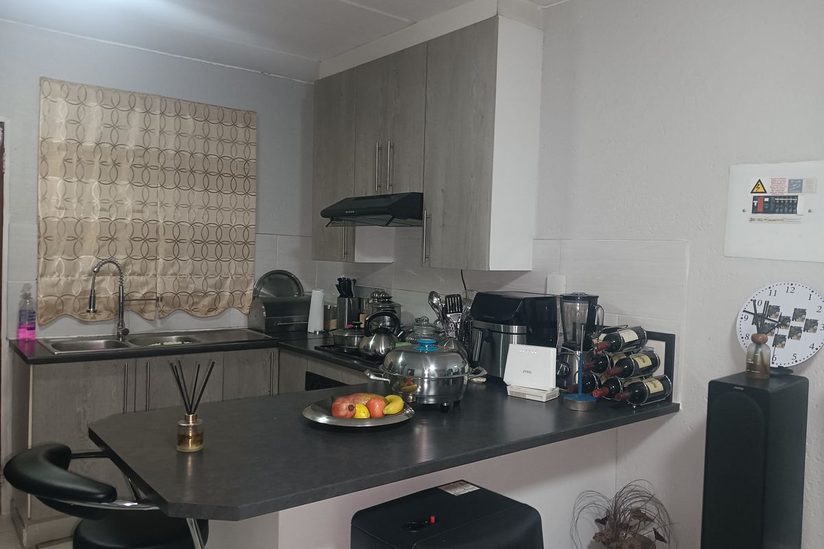 A functional kitchen featuring laminate cabinetry, dark countertops, a stainless steel sink with a gooseneck faucet, and a built-in extractor fan.