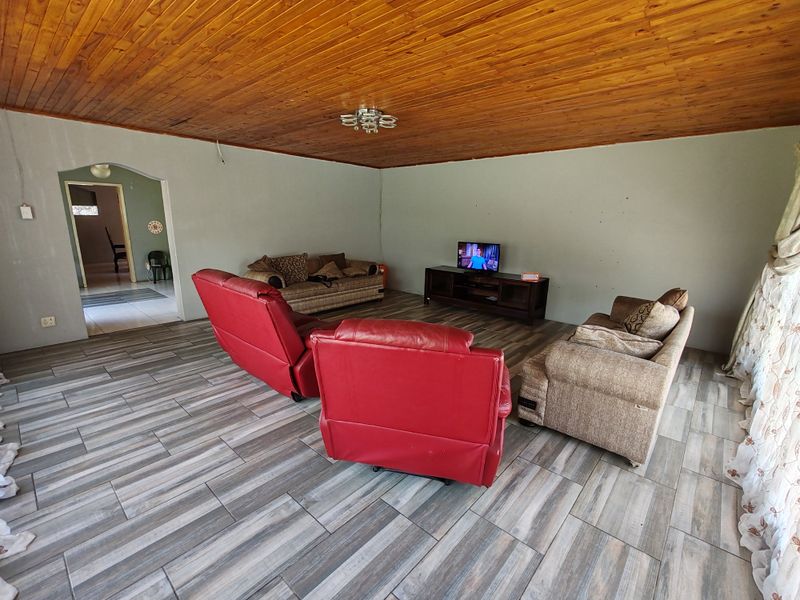 Spacious living room featuring a warm timber tongue and groove ceiling and modern wood-look tiled flooring, leading through an archway to adjacent areas.