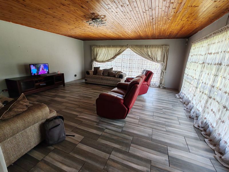 Spacious living room featuring wood-look tiled flooring and a warm timber tongue and groove ceiling, offering a comfortable and inviting atmosphere.
