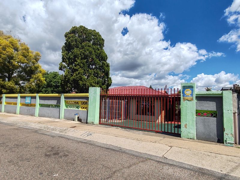 Front exterior view of the property featuring a gated entrance, perimeter wall with security spikes, and a metal roof structure.
