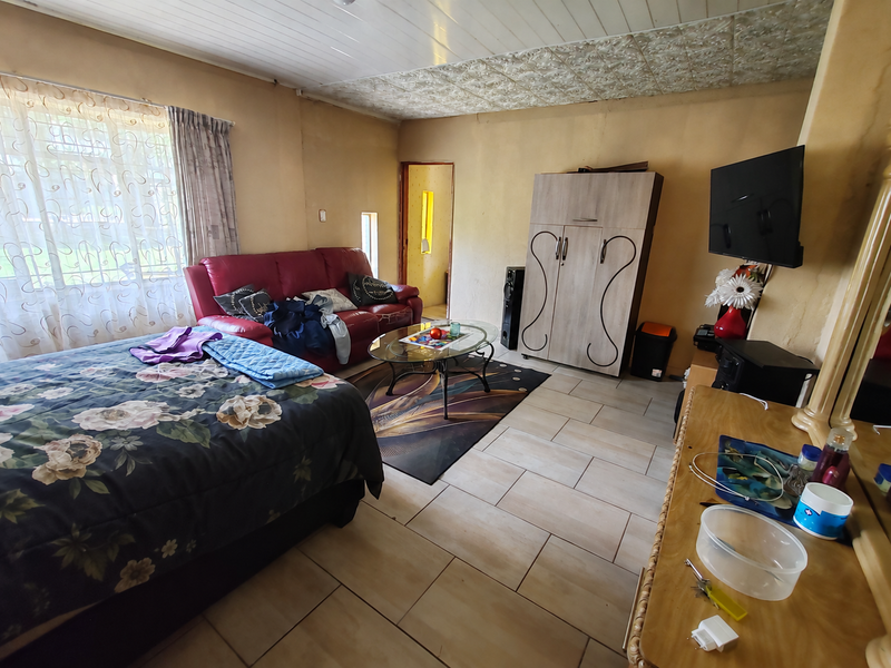 A bedroom featuring tiled flooring and a panelled ceiling, offering a functional space with built-in storage and natural light from the window.