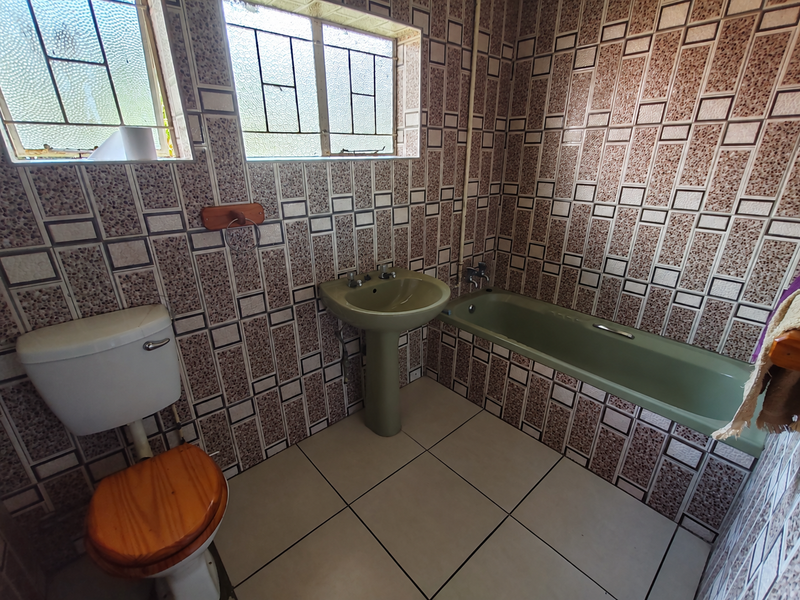 A dated bathroom featuring a pedestal basin, bathtub, and toilet, finished with patterned wall tiles and floor tiles.