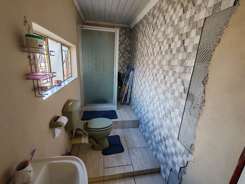 A bathroom featuring a shower enclosure, toilet, and washbasin, currently requiring completion of wall tiling and general maintenance to improve the finish.