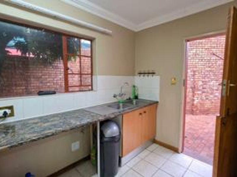 Functional scullery area featuring laminate countertops, stainless steel sink, tiled splashback, and direct access to the rear exterior via a stable door.