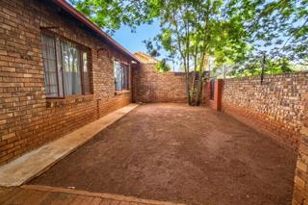 A private rear courtyard featuring face brick walls, a concrete walkway, and an open soil area ready for landscaping or garden development.