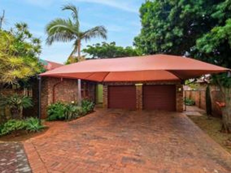 Front exterior view featuring a double garage with a brick driveway and a large shade sail structure.