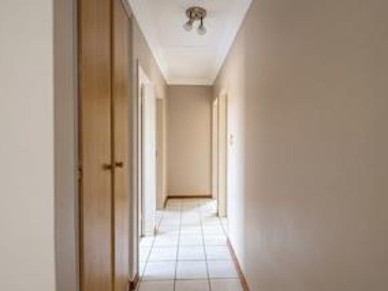A clean and functional hallway featuring tiled flooring, built-in storage cupboards, and neutral wall finishes, providing access to various rooms within the home.