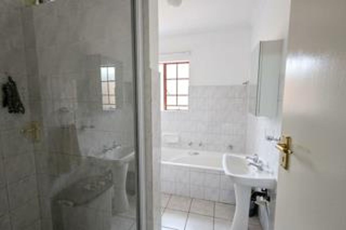 A functional bathroom featuring a pedestal basin, a built-in bathtub, and a separate shower enclosure with tiled finishes throughout.