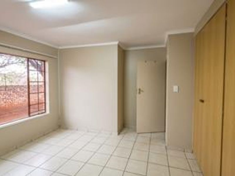 A clean, empty bedroom featuring neutral wall tones, tiled flooring, and built-in wooden cupboards, offering a versatile space ready for personalization.