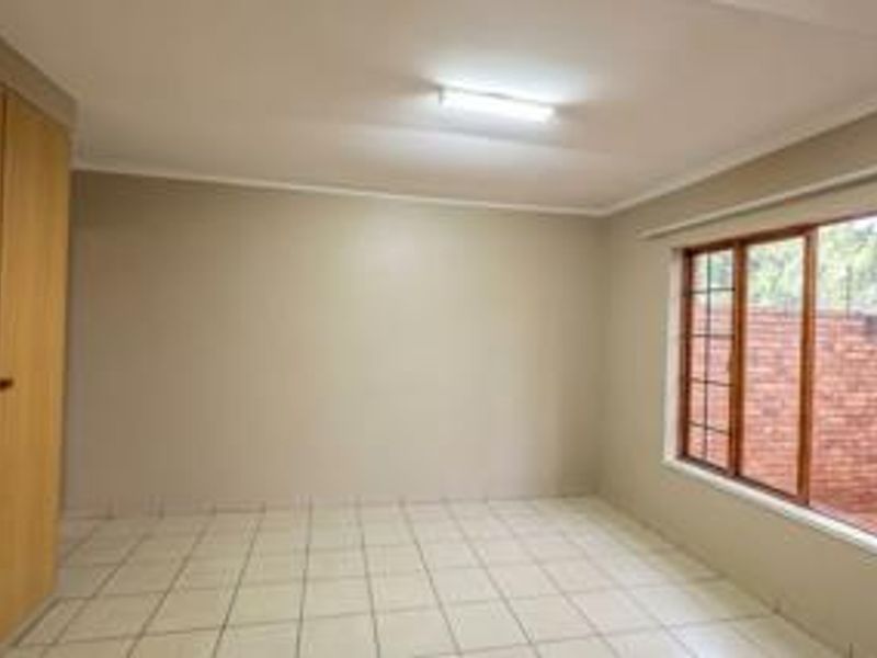 A clean, empty bedroom featuring neutral wall tones, tiled flooring, and built-in wooden cupboards, offering a versatile space ready for personalization.